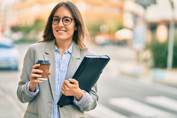 Young hispanic businesswoman drinking coffee holding binder at the city.
