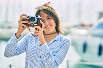 Young hispanic tourist woman smiling happy using vintage camera at the port.