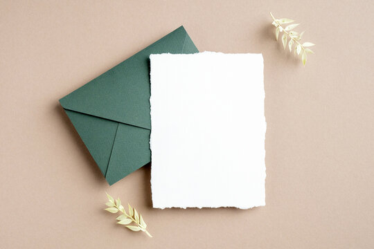 Rustic wedding invitation card mockup, green envelope and dried flowers on pastel beige background. Flat lay, top view, copy space.