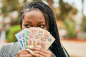 Young african american businesswoman smiling happy covering face with canadian dollars at the park.