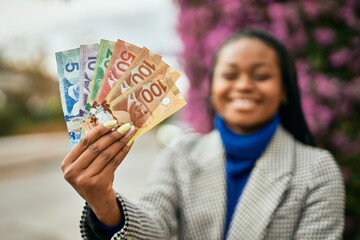 Young african american businesswoman smiling happy holding canadian dollars at the city.