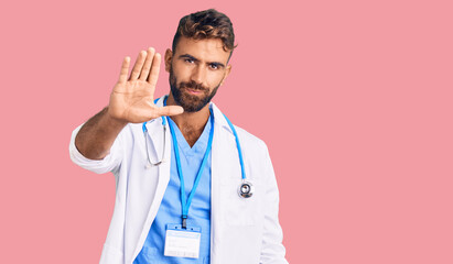 Young hispanic man wearing doctor uniform and stethoscope doing stop sing with palm of the hand. warning expression with negative and serious gesture on the face.