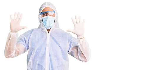 Young hispanic man wearing doctor protection coronavirus uniform and medical mask showing and pointing up with fingers number ten while smiling confident and happy.