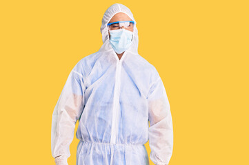 Young hispanic man wearing doctor protection coronavirus uniform and medical mask winking looking...