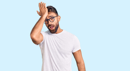 Young hispanic man wearing casual clothes and glasses surprised with hand on head for mistake,...