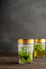 View of two glasses decorated with mint tea, selective focus, on wooden table, gray background, vertical, with copy space