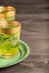 Top view of three decorated mint tea glasses on green plate, selective focus, on dark wooden table, vertical, with copy space