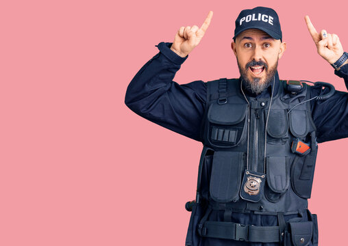 Young handsome man wearing police uniform smiling amazed and surprised and pointing up with fingers and raised arms.