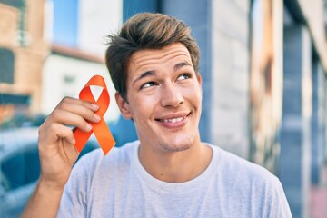 Young caucasian man smiling happy holding orange ribbon at the city.