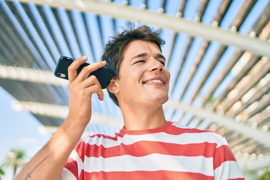 Young caucasian man smiling happy listening audio message using smartphone at the city.