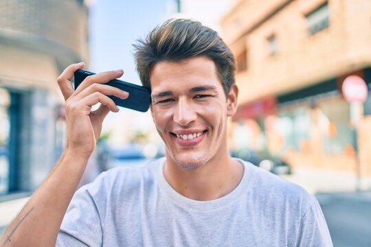 Young caucasian man smiling happy listening audio message using smartphone at the city.