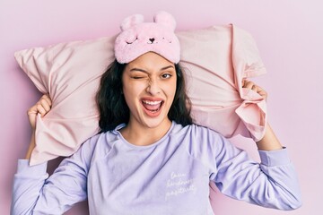 Beautiful middle eastern woman wearing sleep mask and pajama sleeping on pillow winking looking at...
