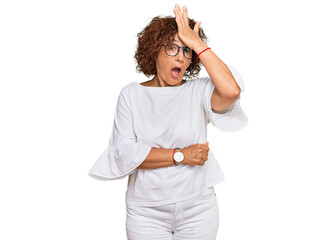 Beautiful middle age mature woman wearing casual clothes and glasses surprised with hand on head...