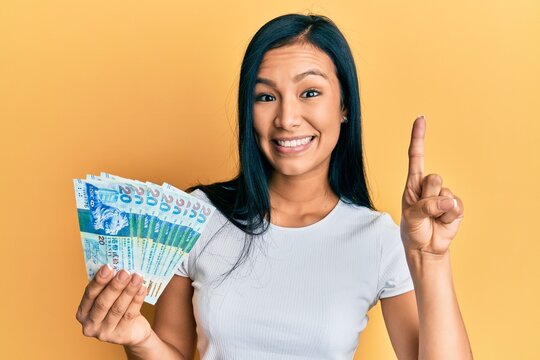 Beautiful hispanic woman holding hong kong 20 dollars banknotes smiling with an idea or question pointing finger with happy face, number one