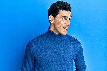 Handsome hispanic man wearing turtleneck sweater looking to side, relax profile pose with natural face and confident smile.