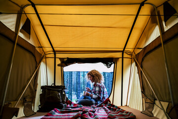 Obraz na płótnie Canvas Travel woman sitting in the auto tent and enjoying outdoors from the window with amazing landscape. Best wake up during adventure trip with feeling. Concept of nature and having freedom in holiday