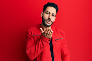 Young hispanic man wearing red leather jacket looking at the camera blowing a kiss with hand on air being lovely and sexy. love expression.