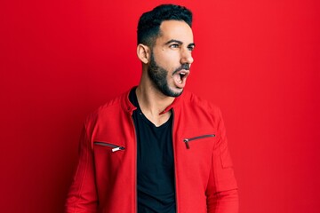 Obraz premium Young hispanic man wearing red leather jacket angry and mad screaming frustrated and furious, shouting with anger. rage and aggressive concept.