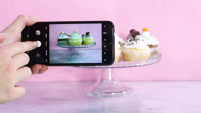 Taking pictures of served cupcakes with white cream with mobile phone