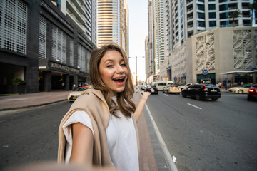 Fototapeta na wymiar Young woman take selfie photo on the phone with modern skycrapers on background. Low angle