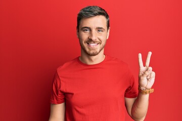 Handsome caucasian man wearing casual red tshirt showing and pointing up with fingers number two while smiling confident and happy.