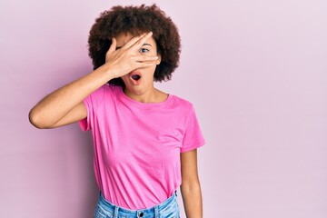 Young hispanic girl wearing casual clothes peeking in shock covering face and eyes with hand, looking through fingers afraid
