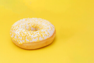 Donut with white sugar glazed and sprinkled with yellow pastry crumbs, on a yellow background with copy space.