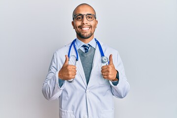 Hispanic adult man wearing doctor uniform and stethoscope success sign doing positive gesture with...