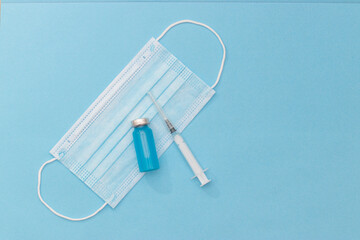 Concept of vaccination against coronavirus, medicine, injections, vaccination against covid-19. Bottle of vaccine on blue medical mask, syringe. Copy space. flat lay.