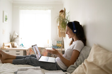 Smiling young woman in headset sit on bed enjoy studying foreign language at online course using...