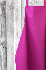 Fuschia kitchen apron on wooden background with copy space