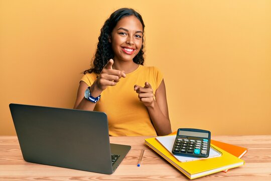 Young african american girl working at the office with laptop and calculator pointing fingers to camera with happy and funny face. good energy and vibes.