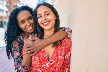African american mother and daughter hugging and smiling happy leaning on the wall.