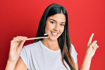 Young brunette woman holding toothbrush with toothpaste smiling happy pointing with hand and finger to the side