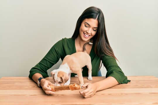 Young hispanic girl smiling happy and playing with dog sitting on the table over isolated white background.