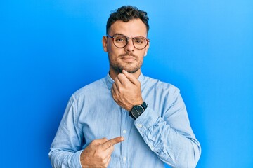 Young hispanic man wearing casual clothes and glasses in hurry pointing to watch time, impatience, looking at the camera with relaxed expression