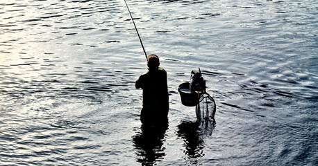 Fisherman catching fish in blue sea at sunset.