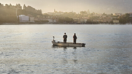 Naklejka premium Fishermen on their boat on Lake Como near Lecco. Malgrate on background