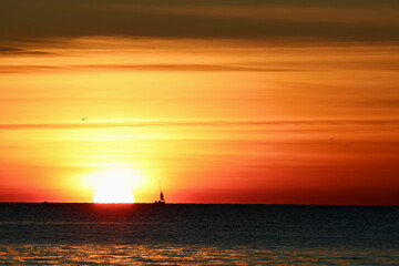 Naklejka na ściany i meble Große Sonne bei Sonnenuntergang mit Segelschiff am Horizont links