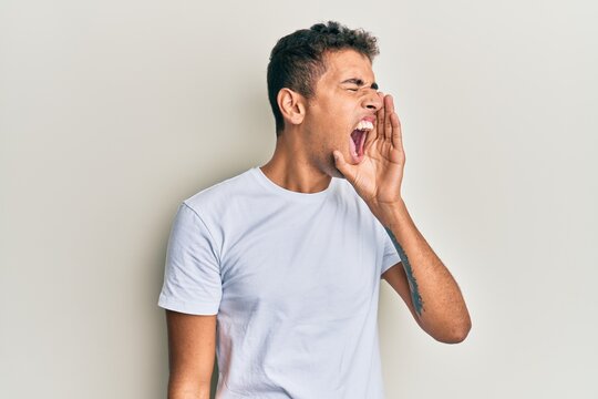 Young handsome african american man wearing casual white tshirt shouting and screaming loud to side with hand on mouth. communication concept.