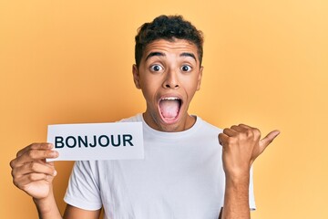 Young handsome african american man holding bonjour french greeting word pointing thumb up to the side smiling happy with open mouth © Krakenimages.com