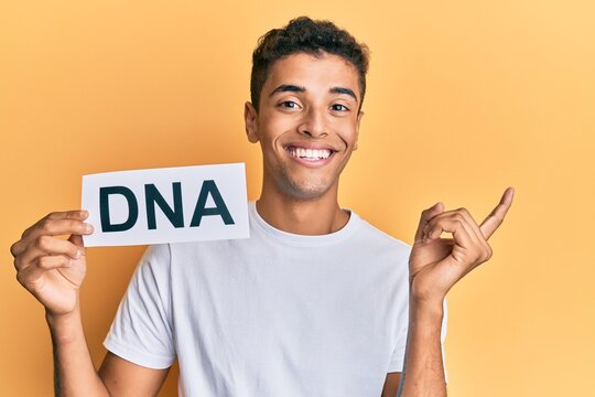 Young handsome african american man holding dna word smiling happy pointing with hand and finger to the side