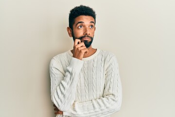 Handsome hispanic man with beard wearing casual winter sweater thinking concentrated about doubt with finger on chin and looking up wondering