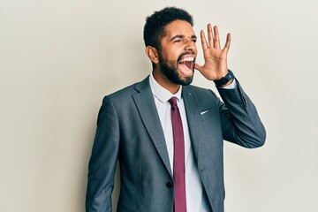 Handsome hispanic man with beard wearing business suit and tie shouting and screaming loud to side with hand on mouth. communication concept.
