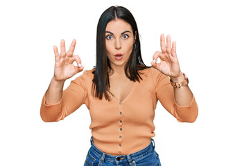 Young hispanic woman wearing casual clothes looking surprised and shocked doing ok approval symbol with fingers. crazy expression