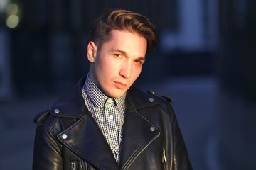 Portrait of serious handsome young man in black leather jacket and shirt staring, looking...