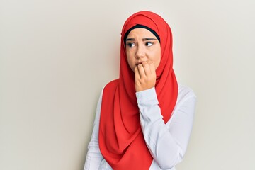 Young beautiful hispanic girl wearing traditional islamic hijab scarf looking stressed and nervous with hands on mouth biting nails. anxiety problem.