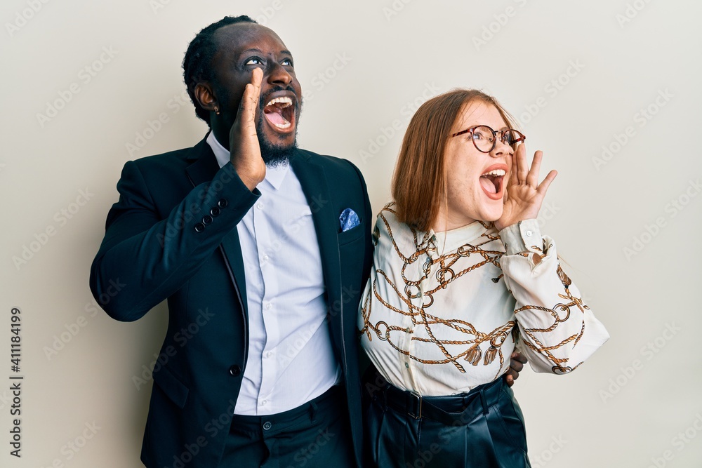 Poster Young interracial couple wearing business and elegant clothes shouting and screaming loud to side with hand on mouth. communication concept.