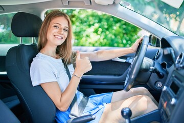 Young beautiful blonde woman smiling happy driving car with thumb up doing ok sign.