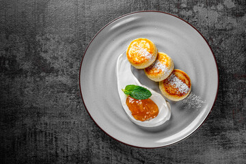 cheese pancakes with sour cream and strawberry sauce on plate on Dark grey black slate background